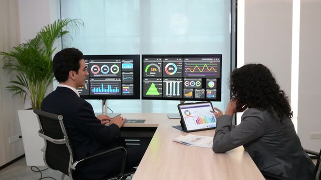 Team of business analysts analyzing financial dashboard charts on dual monitors. Professional colleagues discussing data strategy using digital tablet in modern corporate office. - Powered by Adobe