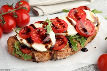 Delicious sandwich with mozzarella cheese, balsamic sauce, tomatoes and arugula on table, closeup