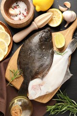 Fresh raw flounder fish, spices and juicer on black wooden table, flat lay. Seafood