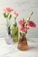 Beautiful eustoma flowers in glass vases on white marble table
