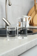 Beakers with clean water near sink on counter in kitchen, closeup