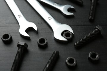 Many metal wrenches, bolts and nuts on black wooden table, closeup