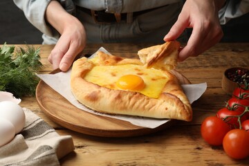 Woman eating delicious khachapuri at wooden table, closeup