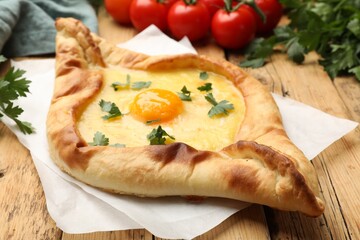 Tasty khachapuri with cheese, egg, tomatoes and parsley on wooden table, closeup