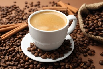 Cup of hot coffee, beans and cinnamon on brown background, closeup