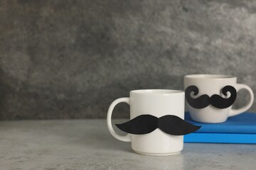Happy Father's Day. Cups with paper moustaches and books on light grey table, closeup. Space for text