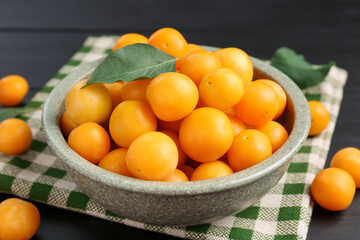 Ripe yellow cherry plums with leaves on black wooden table, closeup