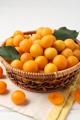 Ripe yellow cherry plums with leaves on white wooden table, closeup
