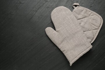 Grey oven glove and potholder on dark textured table, top view. Space for text