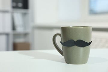 Happy Father's Day. Cup with paper moustache on white table indoors, closeup. Space for text