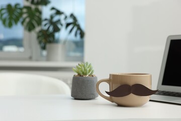 Happy Father's Day. Cup with paper moustache and laptop on white table indoors, space for text