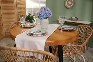 Stylish setting with plates and vase of flowers on wooden table in dining room. Interior design
