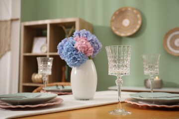 Stylish setting with plates and vase of flowers on wooden table in dining room. Interior design