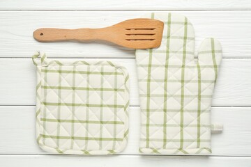 Oven glove, potholder and spatula on white wooden table, flat lay