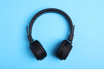 Pair of stylish black headphones on light blue background, top view