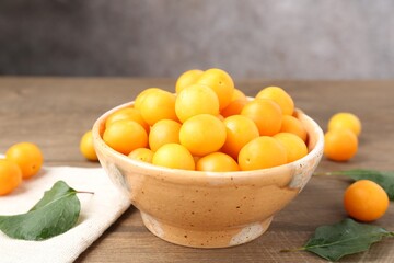 Ripe yellow cherry plums and leaves on wooden table, closeup