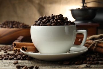 Aromatic coffee beans in cup, cinnamon and grinder on wooden table, closeup