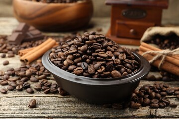 Aromatic coffee beans in bowl and cinnamon on wooden table, closeup