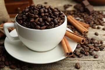 Aromatic coffee beans in cup, cinnamon and pieces of chocolate on wooden table, closeup
