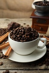 Aromatic coffee beans in cup, cinnamon and grinder on wooden table, closeup