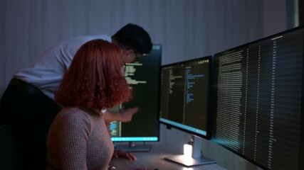 Professional programmers analyzing code on multiple monitors in dark office. Man and woman developers collaborating on cybersecurity project late at night in modern technology workplace. - Powered by Adobe