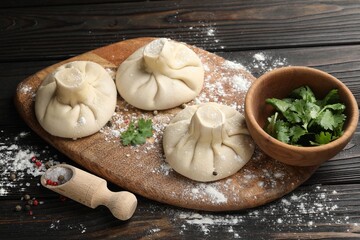 Uncooked khinkalis (dumplings), spices and parsley on dark wooden table, closeup