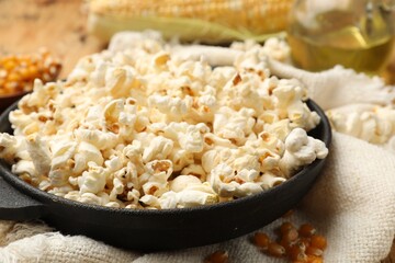 Tasty popcorn, corn kernels, oil and towel on wooden table, closeup