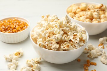 Tasty popcorn and corn kernels on white table, closeup