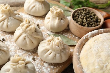 Uncooked khinkalis (dumplings) with peppercorns, flour and bay leaves on wooden table, closeup