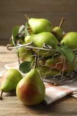 Fresh ripe pears in metal basket and green leaves on wooden table, closeup