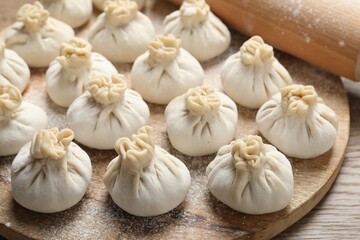Uncooked khinkalis (dumplings) and rolling pin on wooden table, closeup