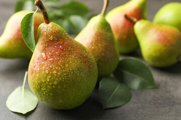 Fresh ripe pears and green leaves on grey table, closeup