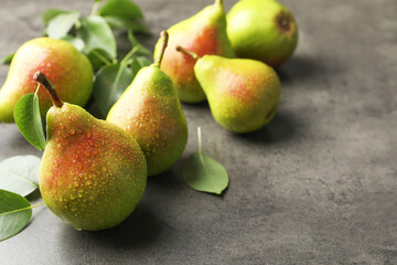Fresh ripe pears and green leaves on grey table, closeup. Space for text