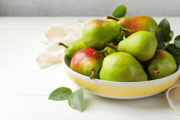 Fresh ripe pears in bowl and green leaves on white wooden table, closeup. Space for text