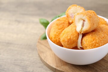 Delicious fried croquettes in bowl and basil on wooden table, closeup. Space for text