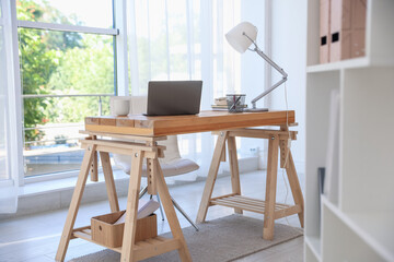Home workspace. Laptop and stationery on wooden desk near window indoors