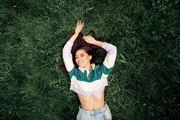 Joyful woman smiling while lying on a grassy field outdoors, wearing a casual sweatshirt, enjoying a relaxing day in nature