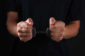 Man in metal handcuffs on black background, closeup