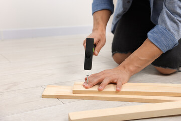 Man hammering nail into wooden plank indoors, closeup. Space for text