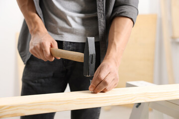 Man hammering nail into wooden plank indoors, closeup
