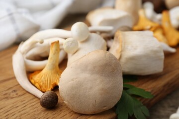 Different raw mushrooms and parsley on wooden table, closeup