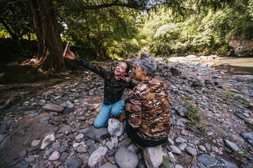 Mother and daughter taking photos next to their newly built apacheta next to the river, smiling and enjoying the moment.