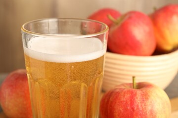Delicious cider in glass and apples on blurred background, closeup