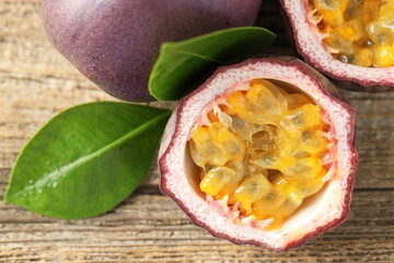 Fresh passion fruits and green leaves on wooden table, flat lay