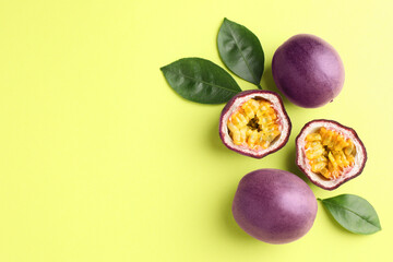 Fresh passion fruits and leaves on pale green background, flat lay. Space for text
