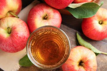 Delicious cider in glass, apples and leaves on wooden table, flat lay