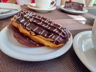 Chocolate eclair pastry with cream filling on a white plate. Concept of sweet dessert, bakery product, celebration treat, and food advertising.