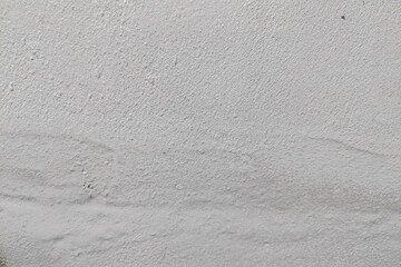 Close-up texture of a rough concrete wall with old plaster, cracks, and peeling surface, showing weathered construction material detail for background or design use.
