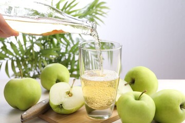 Woman pouring fresh cider into glass at table, closeup
