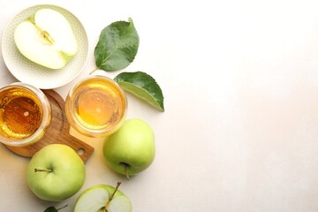 Fresh cider in glasses, apples and green leaves on beige table, flat lay. Space for text